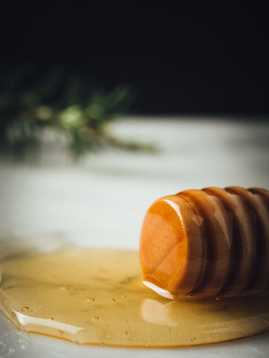 A vertical closeup shot of a wood dipper of honey and honey leaking from it on  a white surface