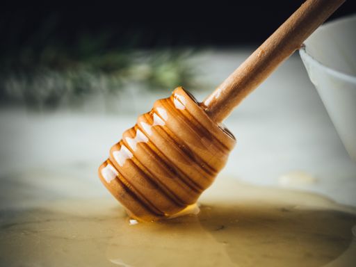 A honey wood dipper is dripping honey on a white marble surface