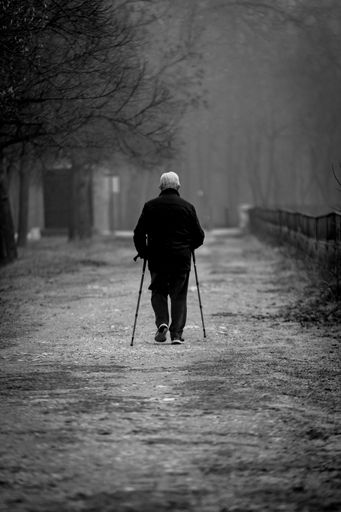 An older man, walking with two canes down the path in the park, during the winter day, in grayscale, the concept of aging and solitude