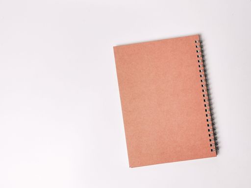 A brown spiral notebook lying flat on a white surface.