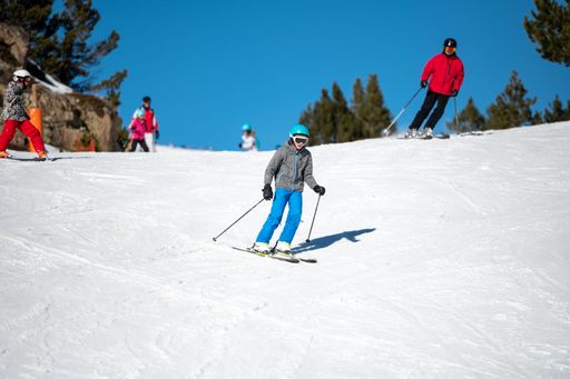 A group of people skiing down a snow-covered mountain slope on a bright, sunny day