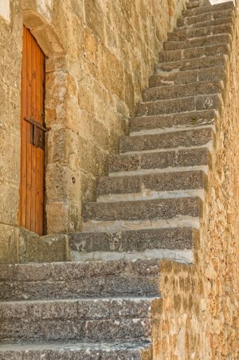 A view of stairs in front of an old wooden door in a stone wall in Denia, Spain