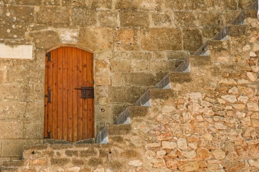 A view of stairs in front of an old wooden door in a stone wall in the scenic city of Denia, Spain