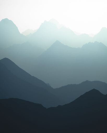 A vertical shot of the bluish silhouettes of mountains in sunlight.
