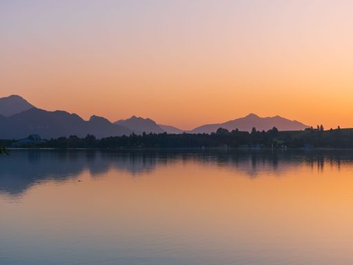 A peaceful scenery of a lake with mountain silhouettes in the background during the sunset
