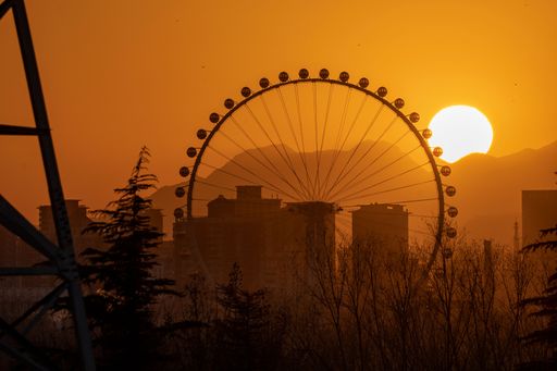 An iconic ferris wheel looms in the skyline of a bustling metropolis, the perfect frame for a stunning sunset