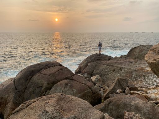 A beautiful view of a man standing in the cliff in the beach during sunset