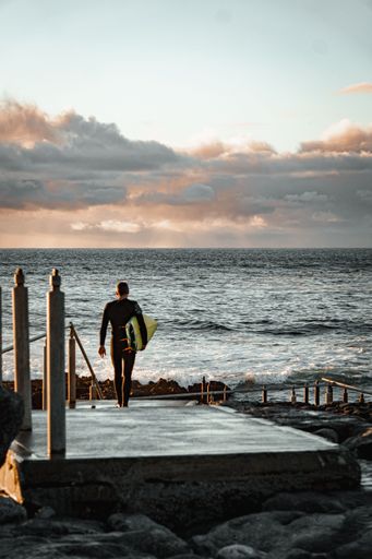 A beautiful view of a surfer standing in the cliff in the beach during sunset