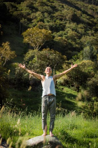 A handsome young man in a white t-shirt happily throwing his hands in the air in the field
