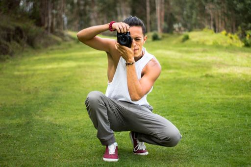 A handsome young man in a ponytail and a white t-shirt taking a picture in the field on a sunny day