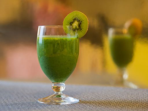 A closeup shot of a glass of kiwi smoothie decorated with a kiwi slice with a blur mirrored background