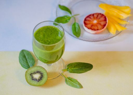 A top view of a glass of kiwi smoothie, half of a kiwi, green mint leaves and fruit slices in a plate on a table
