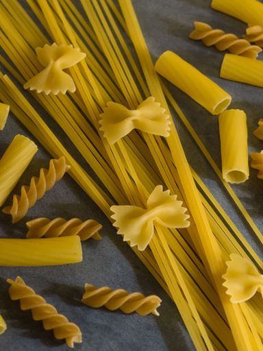 A vertical closeup shot of different types of raw pasta spagetties