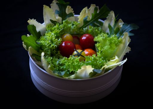 A closeup of a green salad mix with cherry tomatoes in the middle of a white bowl isolated on a black background