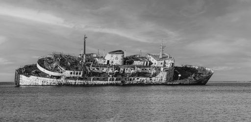 A rusty abandoned ship in the sea under gray cloudy sky, grayscale shot
