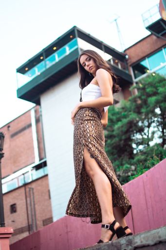 A low angle shot of a brunette female wearing a long skirt with side split and a white crop top outdoors