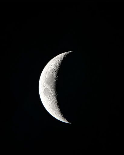 A black-and-white vertical shot of the half Moon shining in the darkness