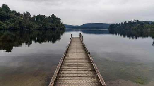A scenic view of a beautiful landscape with mountains and a lake seen from a wooden dock