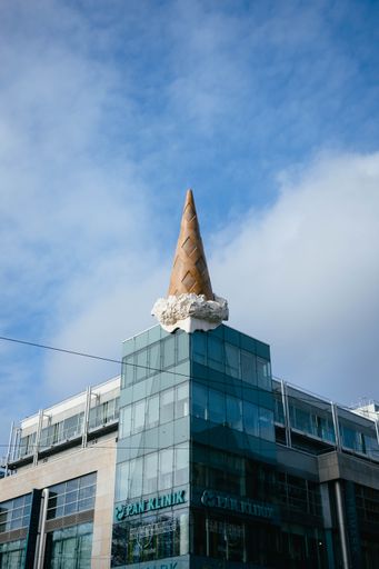 Vertical shot of a giant ice cream cone on a glass building. The scoop of ice cream melts in the sun. In summer there are chocolate and vanilla.