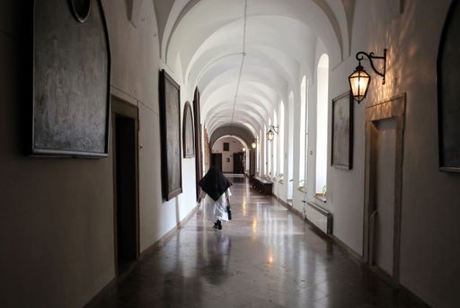 A female adult wearing a black hijab walking down a corridor lit up by a bright light at the end