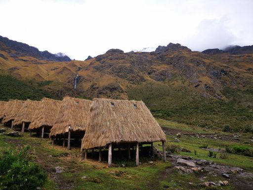 A scenic vista of a countryside landscape featuring numerous thatched roof homes in the foreground, with majestic mountain peaks in the background