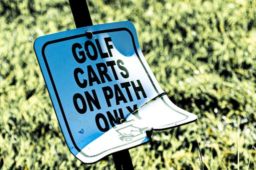 A white sign with "GOLF CARTS ON PATH ONLY" written on it in faded black lettering