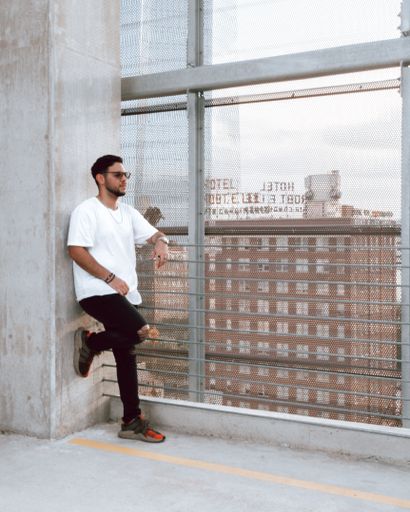 A young guy standing outside behind the window with the city in the background