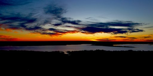 A panoramic shot of a scenic skyline with clouds over a lake at sunset