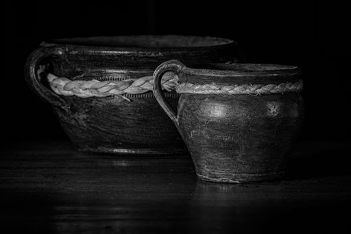 A grayscale of two old beautiful clay pots on a dark background