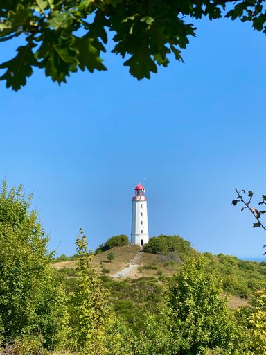 A Lighthouse on Hiddensee Island atop a hill, overlooking a lush landscape of trees and grass against a blue sky