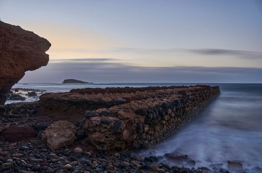 A rocky beach and the ocean near a cliff face, illuminated by the golden light of the setting sun