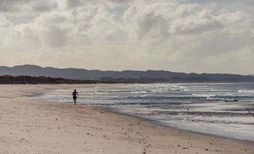 Waipu, Northland New Zealand, August 12 2014. A lone athlete runs along a deserted surf beach on Bream Bay, 