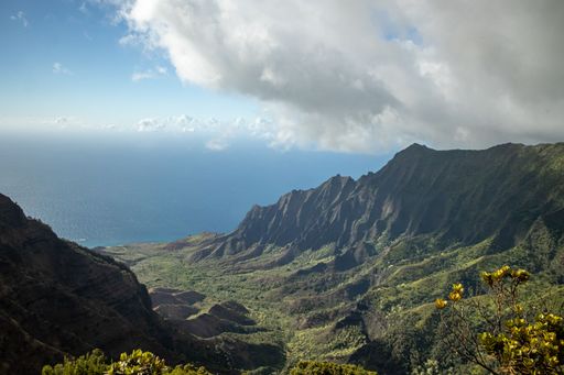 A drone shot of green-covered hills on the coast under the cloudy blue sky