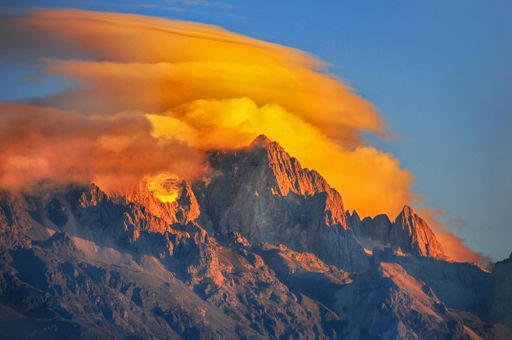 A scenic shot of the peak of a high mount covered with fiery clouds