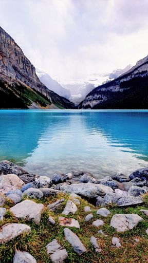 A vertical shot of azure surface of a lake surrounded by rocky hills under the cloudy sky