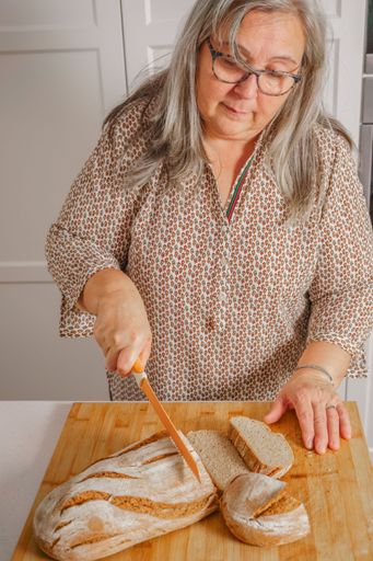white-haired woman cutting slices of freshly baked homemade bread