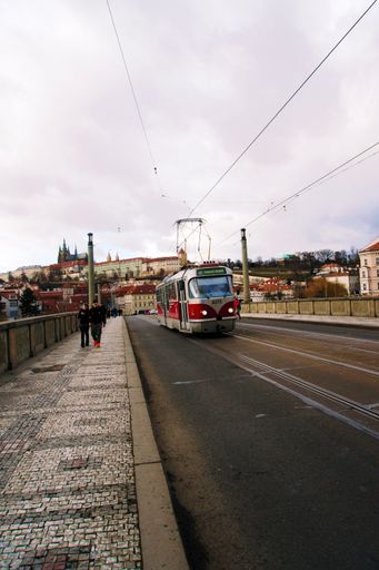 A vertical shot of the people walking along the Manes Bridge in Prague, Czech Republic with the tram passing by in the afternoon