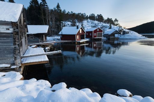 A picturesque winter landscape featuring a group of rustic log cabins set against a tranquil lake partially covered in snow