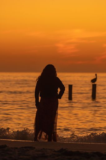 A portrait of the silhouette of a lady standing on a beach staring at the sea dusk dusk