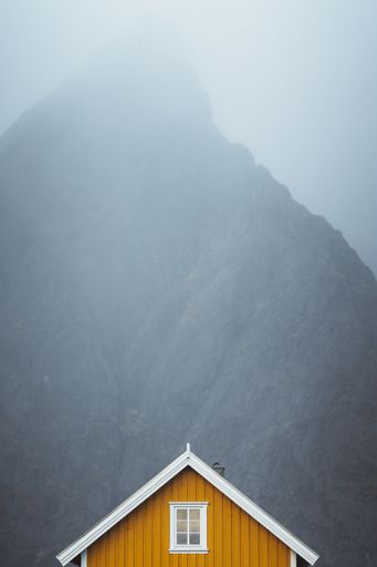 A vertical shot of a wooden cabin with a rocky mountain in a foggy background