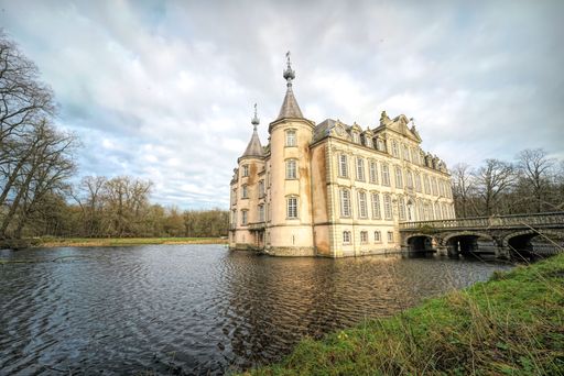 A beautiful view of a bridge to Poeke Castle, near Poeke in the Belgian province of East Flanders, surrounded by trees and a lake, on a cloudy day