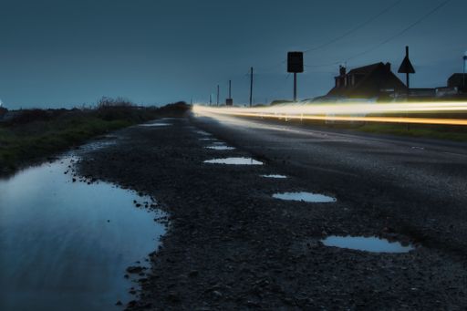 An evening scene featuring illuminated street and traffic signs surrounded by puddles of water