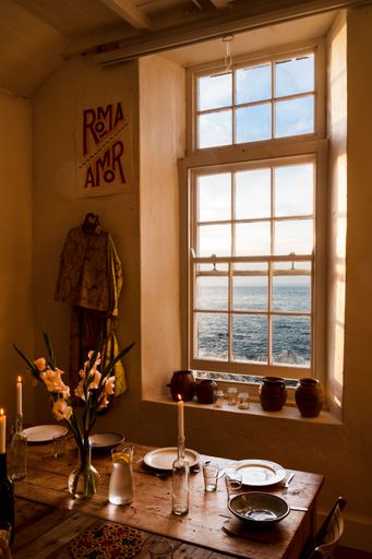 A vertical shot of a living room with a wooden table with a window overlooking the sea
