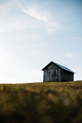 A vertical low angle shot of an old wooden barn in a green field under the blue sky