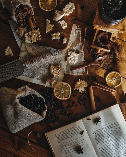 A vertical top view of a wooden table with an open book dried fruits and coffee