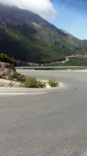 A vertical shot of curvy road near high green hills under blue sky on sunny day