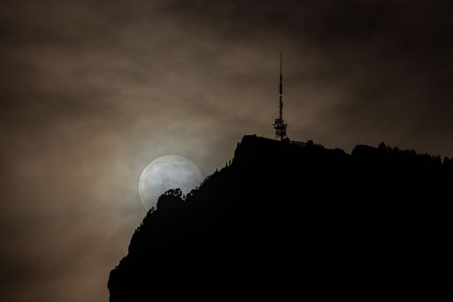 A mystical view of a stunning full moon over an antenna tower on top of the Niederhorn mountain