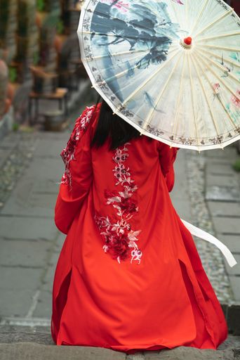 A vertical shot of a geisha walking in the street with a red dress and umbrella - shot from back