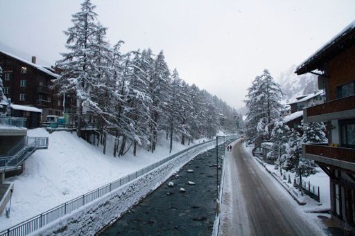 A beautiful winter scene with a frozen river surrounded by snow-covered pine trees and apartment buildings in Interlaken, Switzerland