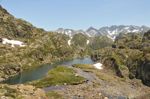 A beautiful view of a serene lake surrounded by green fields and snowy mountains in the Catalan Pyrenees